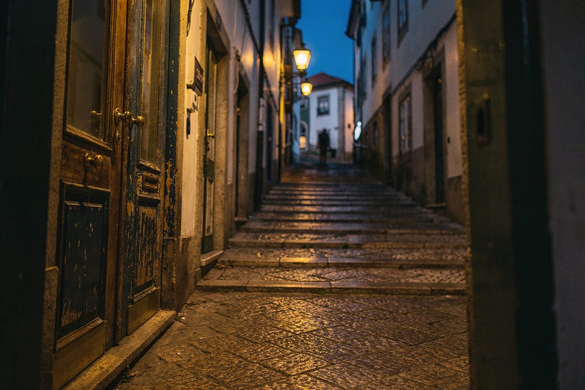 Rua inclinada do Porto ao anoitecer com portas de entrada de madeira